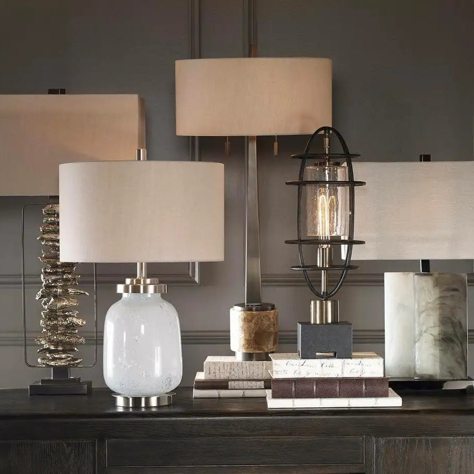 A sleek, frosted white glass table lamp with a brushed metal base and a cylindrical off-white fabric shade.