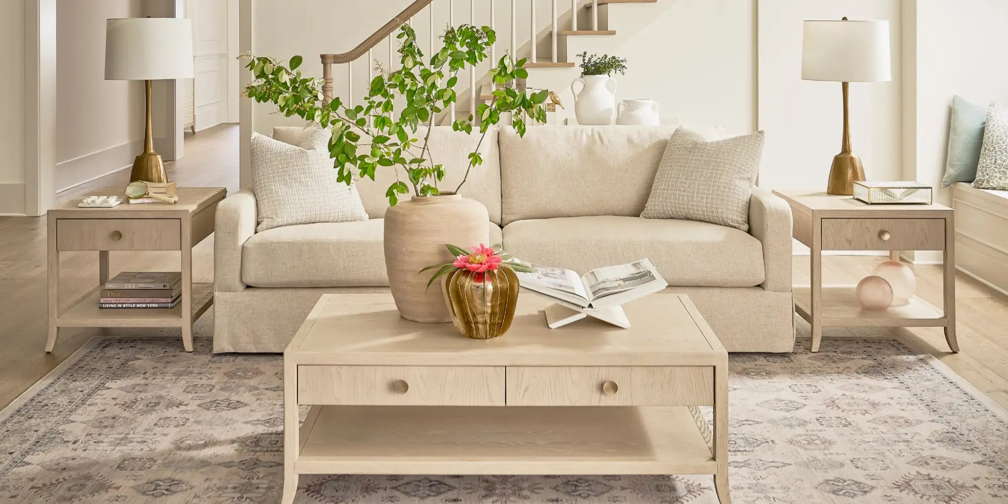 Beige upholstered sofa with matching side tables and a central coffee table, featuring light wood finishes and subtle decorative accents.