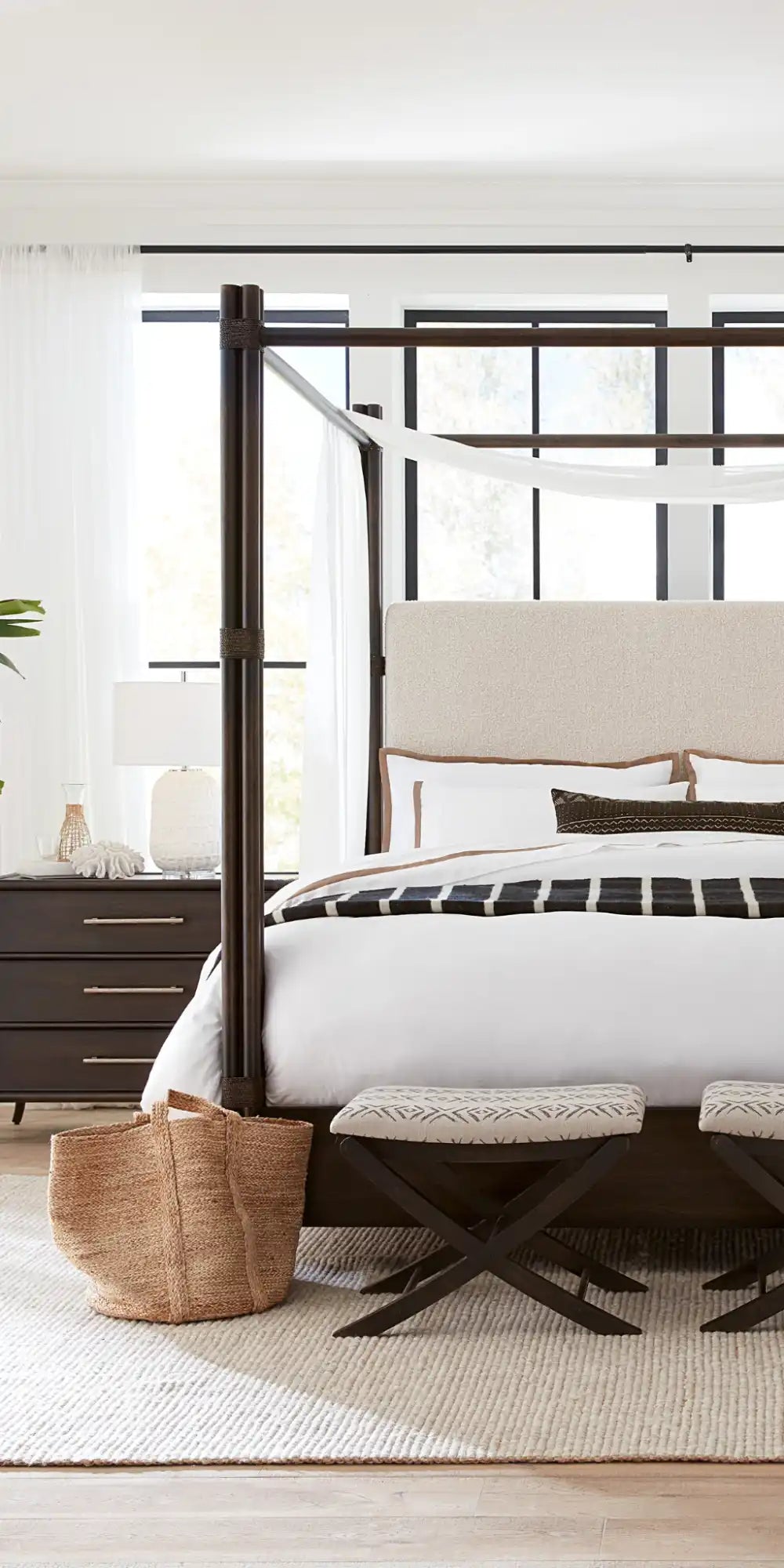 A dark wood four-poster bed with a light-colored upholstered headboard and white bedding.